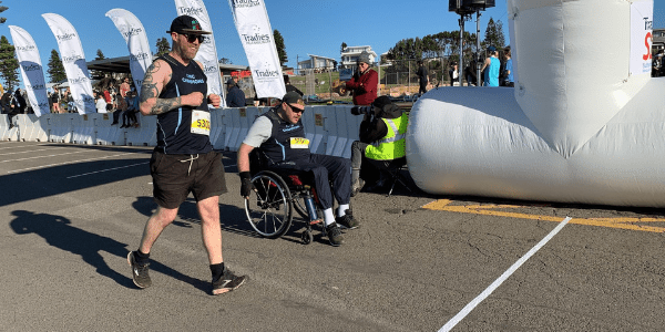 Image shows Civic Champion in wheelchair crossing the finish line of the Sutherland to Surf with Civic volunteer